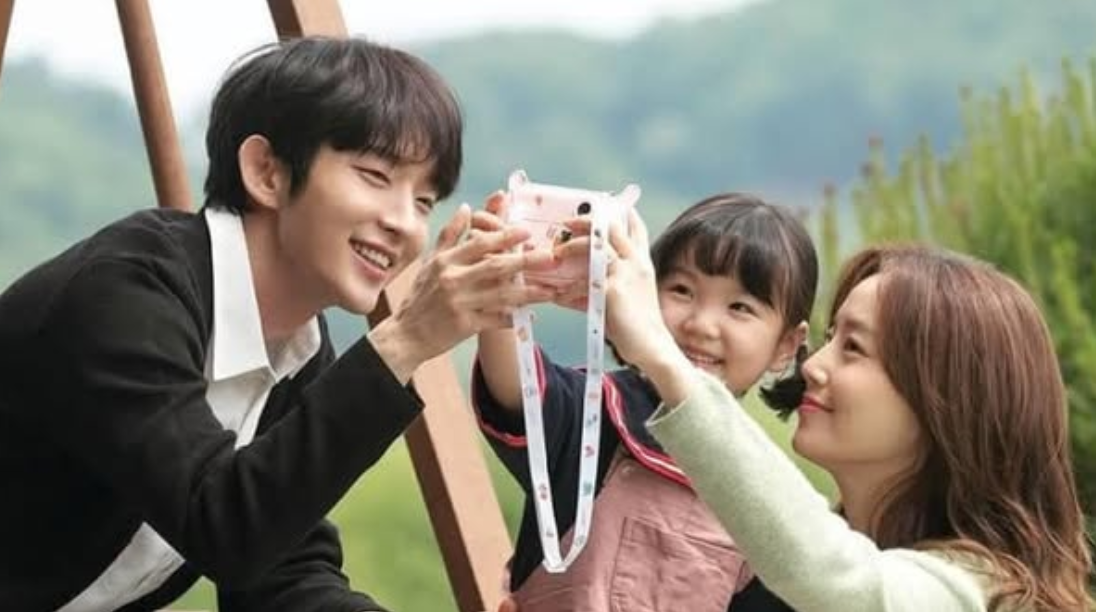 Heartwarming scene from the K-drama "Flower of Evil" showing a smiling man, woman, and young girl happily taking a photo together outdoors. Featured on Top Honest KDrama Review Sites.