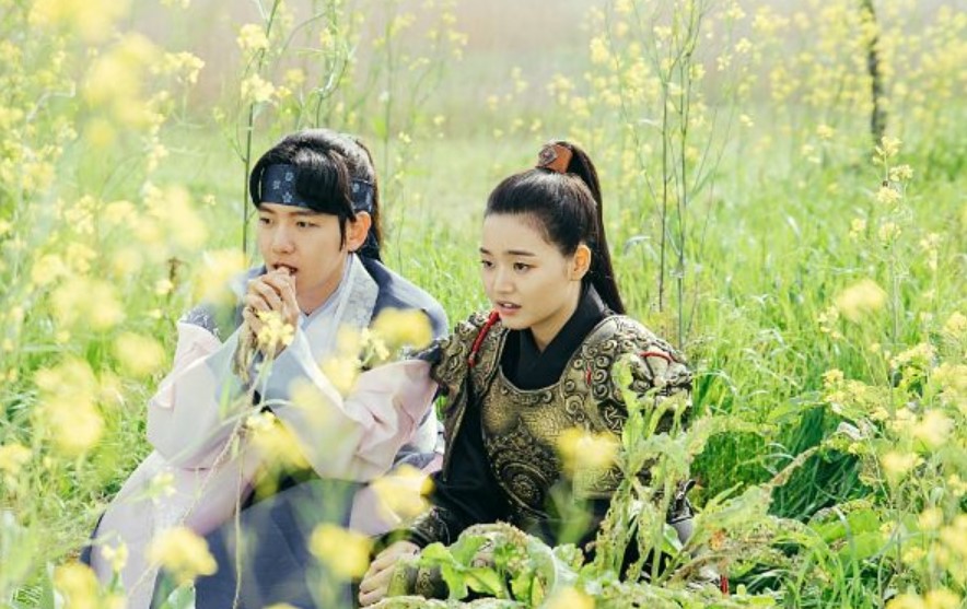 Moon Lovers: Scarlet Heart Ryeo emotional moment between the characters, with one wearing traditional robes and the other in warrior armor, as they sit together in a field of yellow flowers, sharing a tender and vulnerable moment