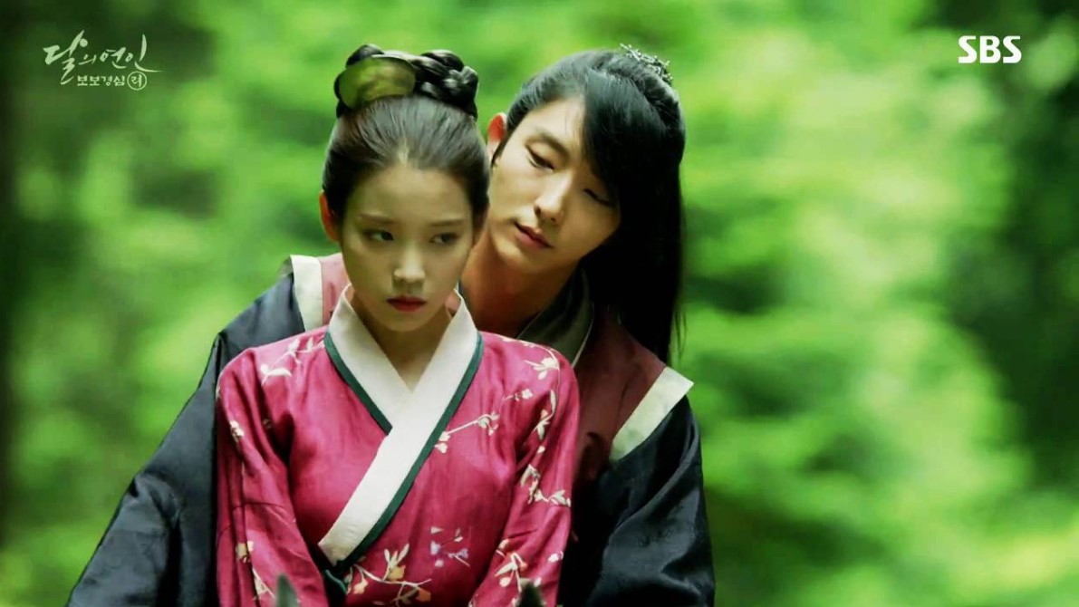 Moon Lovers: Scarlet Heart Ryeo romantic moment between IU and Lee Joon-Gi in a serene forest setting, as Lee Joon-Gi embraces IU from behind, conveying deep affection and emotional tension.