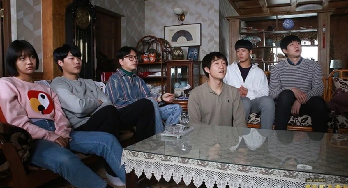Group of friends from Reply 1988 sitting together, capturing a moment of shared connection and emotion in a cozy living room setting.