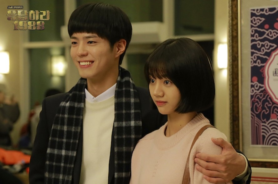 Two main characters from Reply 1988 posing together with smiles, capturing a moment of happiness and closeness in a celebratory setting.