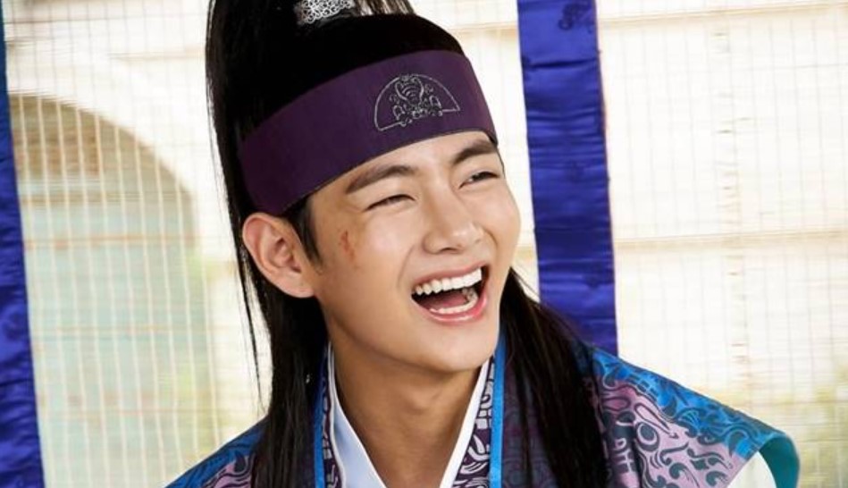 A joyful moment from Hwarang, featuring one of the main characters smiling widely. His face shows a charming expression, with a light scar on his cheek, adding depth to his youthful and carefree personality. He is dressed in traditional hanbok, showcasing the vibrant style of the series.