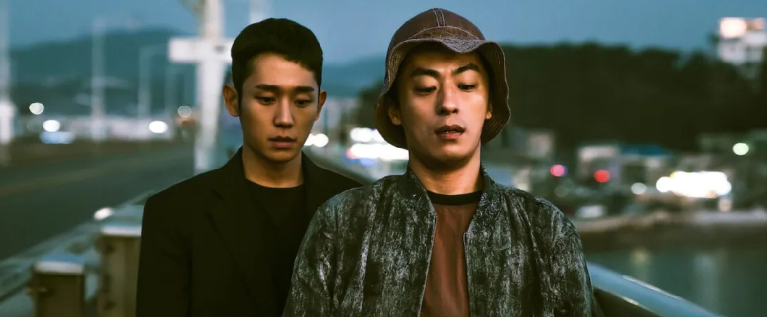 DP Season 1 scene showing two characters, one in military uniform and the other in casual wear, standing on a bridge at night. The serious expressions on their faces reflect the tense relationship and emotional conflict explored in the drama. This image captures a pivotal moment in DP Season 1.