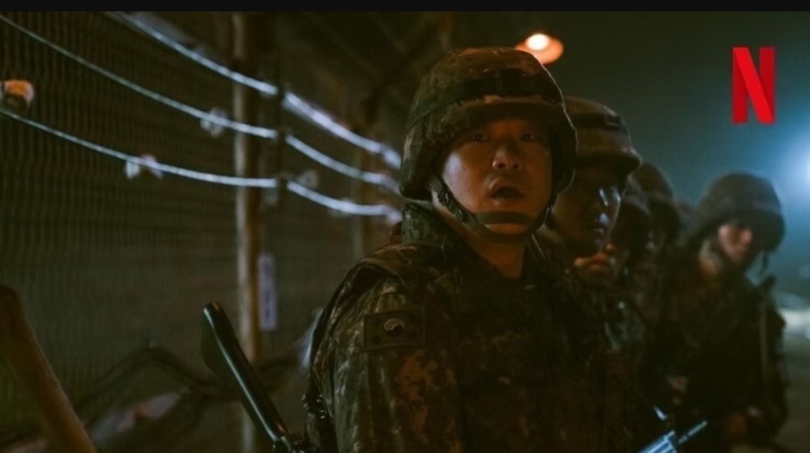 A soldier in full military gear, looking alert and surprised. The backdrop shows a dark, tense environment with barbed wire, and other soldiers are positioned behind him. The iconic Netflix logo is visible in the top right corner