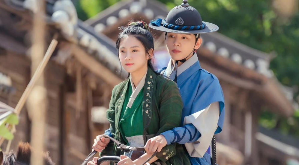 Scene from The Forbidden Marriage featuring the female lead in green attire riding in front of the male lead in traditional blue robes, both captured in a joyful moment with a picturesque traditional Korean village in the background.