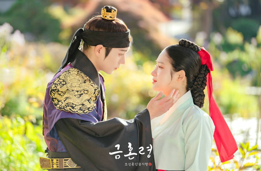 Tender moment from The Forbidden Marriage showing the male lead in royal attire gently holding the female lead’s face, with a soft, romantic atmosphere created by the natural background and golden sunlight.