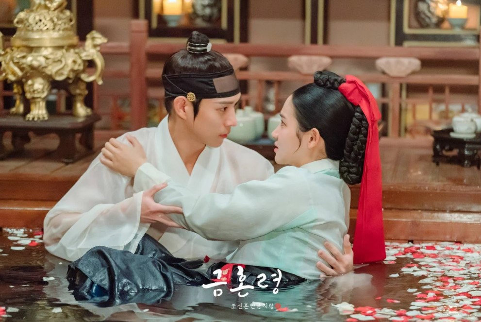 Romantic scene from The Forbidden Marriage featuring the male and female leads in a water-filled setting, surrounded by rose petals, sharing an intimate moment in traditional Korean attire.