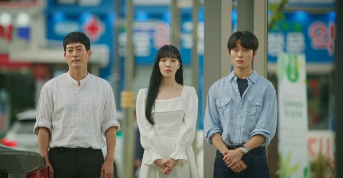 A scene from The Delivery Man, featuring three main characters standing together on a street. The man on the left appears calm, the woman in the middle looks worried, and the man on the right seems tense. The vibrant city backdrop adds a dynamic feel to the moment.