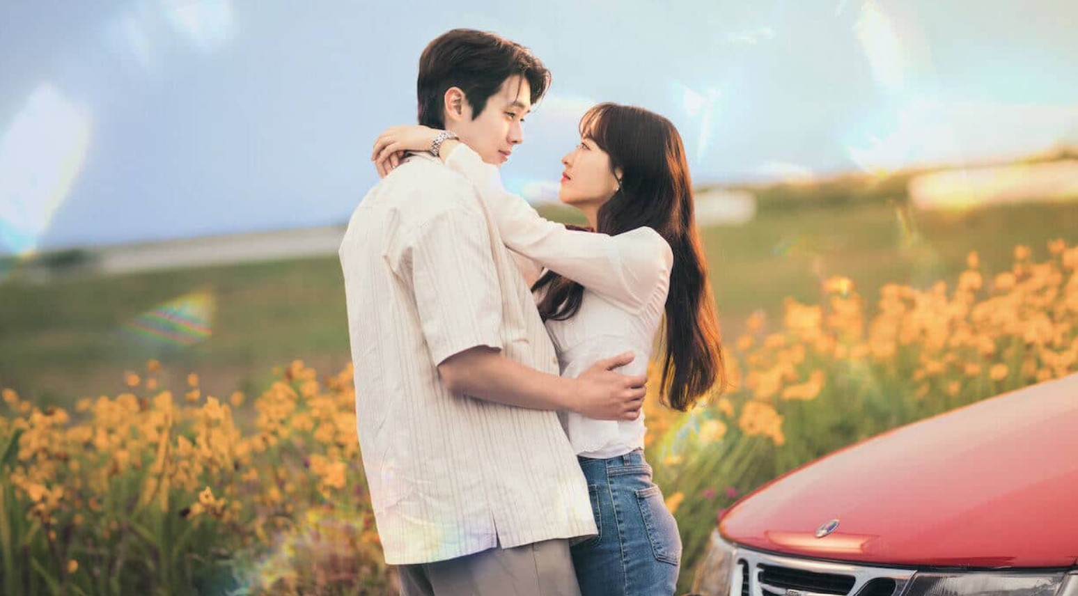 A romantic scene from the K-drama Melo is My Nature, showing a couple in a field of flowers, gazing into each other's eyes near a red car. Featured in Best K-Drama Reviews 2025