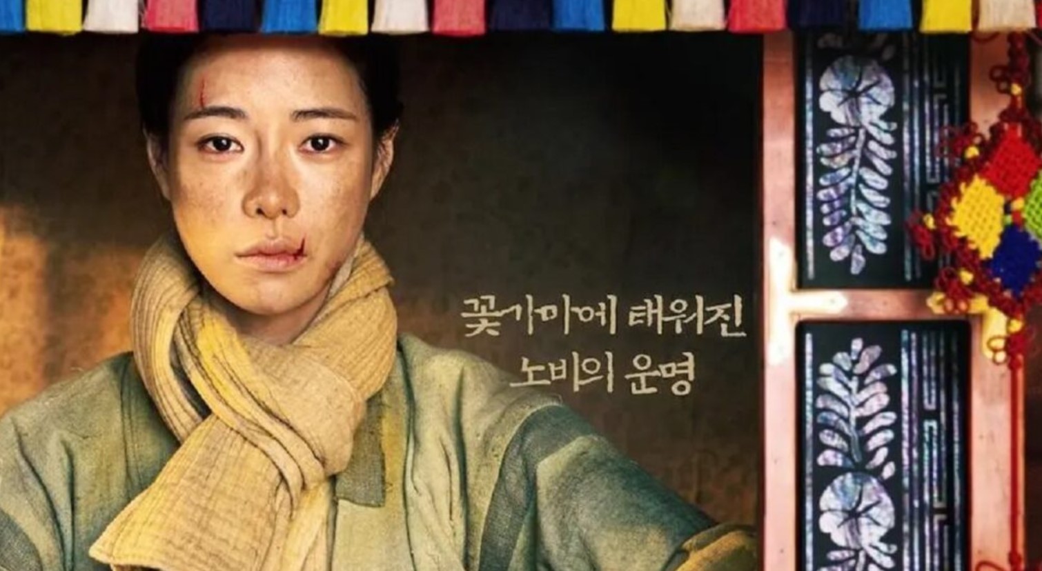 A powerful image from The Tale of Lady Ok, showing the main character with a scar on her face, wearing a yellow scarf, and standing in front of traditional Korean decor. The image reflects the drama's intense and historical themes.