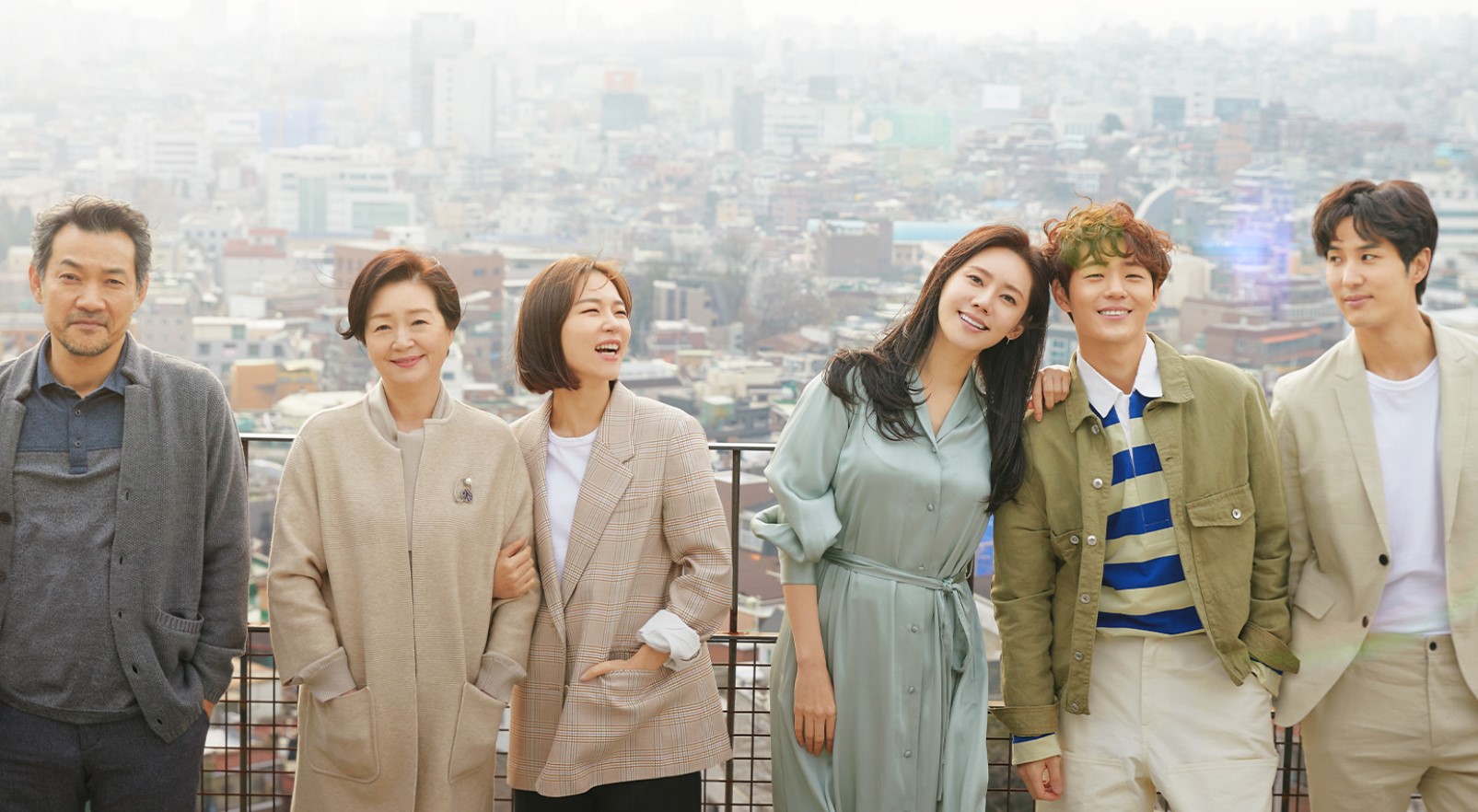 Heartwarming group photo of the cast from the Korean drama My Unfamiliar Family, showcasing the main family members. The scene captures their joyful and loving moments together, with a beautiful cityscape backdrop. One of the most underrated Korean dramas that explores family bonds, misunderstandings, and emotional growth.