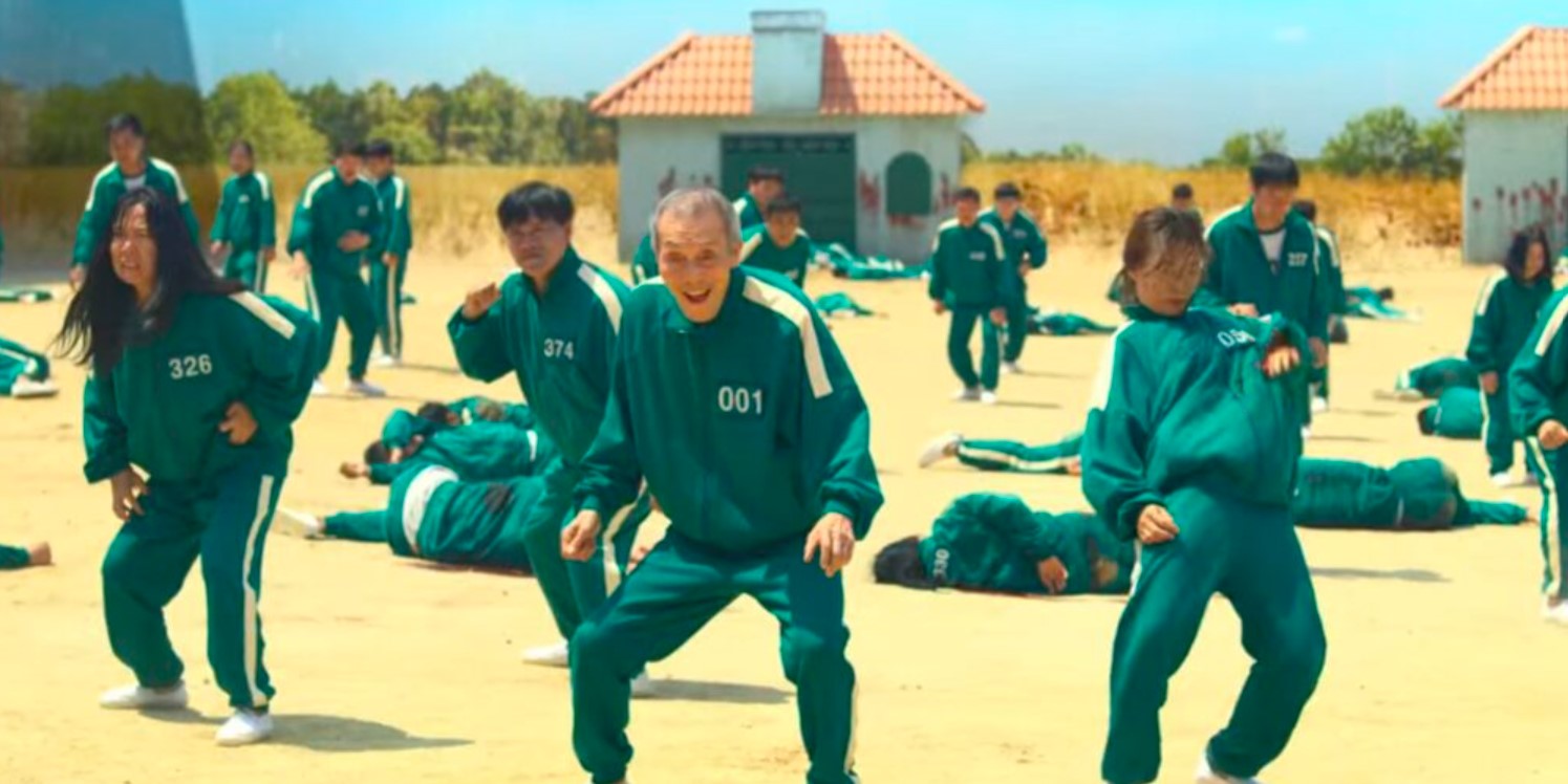 Contestants from Squid Game Season 1, in their green tracksuits, are seen in a tense moment of the game. The elderly character, numbered 001, grins amidst the chaos while others, including contestants numbered 326 and 374, are caught in the action. The intense atmosphere of survival and competition is captured against the backdrop of surreal game settings, perfect for a Squid Game season 1 full review
