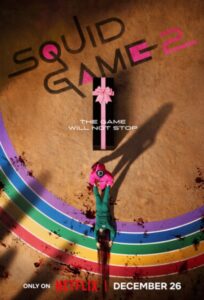 Squid Game Season 2 full review - dramatic poster featuring a rainbow-colored background, a pink gift box, and a bloodied scene with a character in a green tracksuit, showcasing the game's relentless nature.