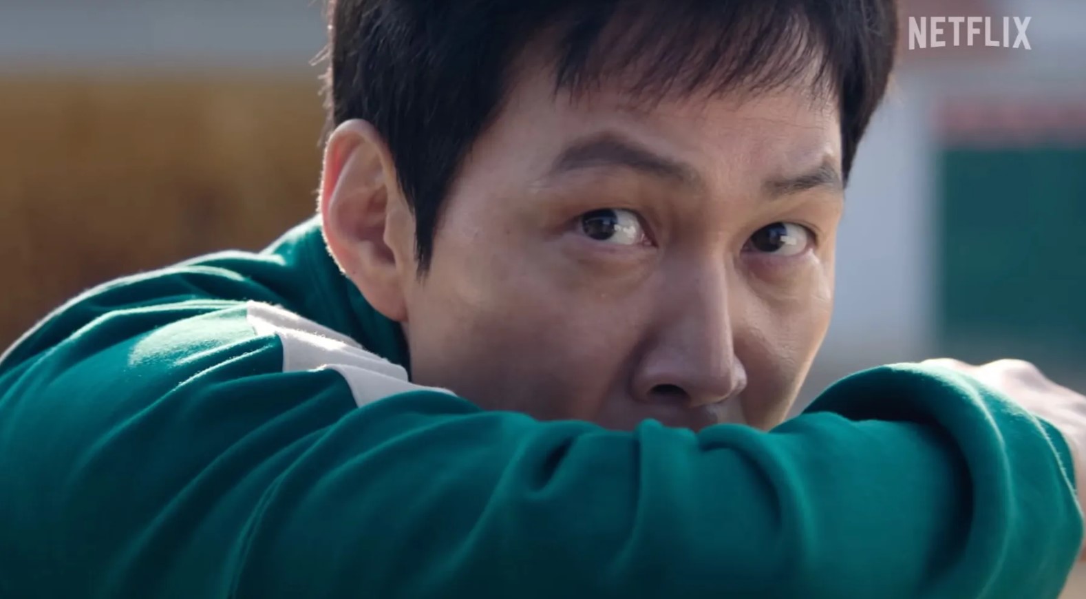 Squid Game Season 2 full review - close-up of a character in a green tracksuit with intense eyes, showcasing the suspenseful and high-stakes atmosphere of the series.