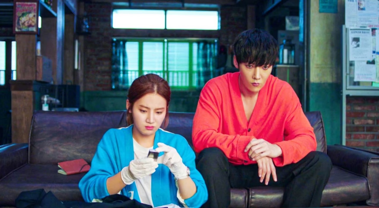 Zombie Detective K-Drama scene with the male and female leads sitting together, deep in thought, in an office-like setting.