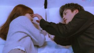 Romantic scene from Doom at Your Service showing a couple lying on a bed as the male lead gently touches the female lead's face