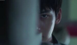 Kim Je Ha (Ji Chang Wook) in a tense moment from The K2, peering through a gap with a focused and intense gaze, highlighting the drama's suspenseful atmosphere.