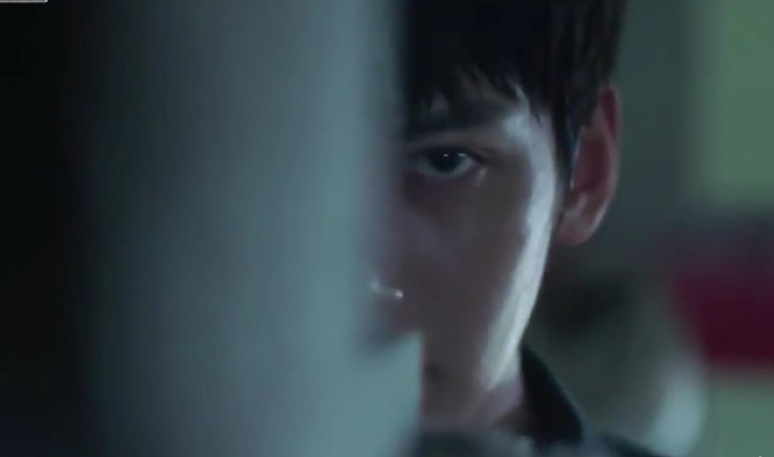 Kim Je Ha (Ji Chang Wook) in a tense moment from The K2, peering through a gap with a focused and intense gaze, highlighting the drama's suspenseful atmosphere.