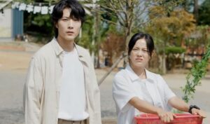 A moment from "Drinking Solo", with the male and female leads standing side by side in a scenic outdoor setting. The male lead looks serious while the female lead gives a playful, slightly confused expression, capturing their contrasting personalities.