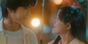 A romantic moment from "Drinking Solo", with the male and female leads sharing a tender gaze under an umbrella in the rain, surrounded by soft glowing lights, highlighting their connection.
