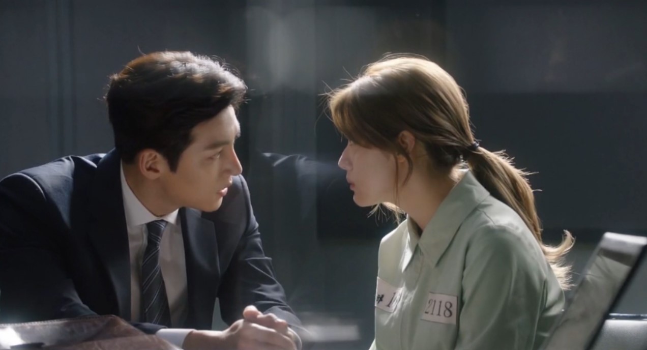 A tense scene from Suspicious Partner, where the male lead, in a suit, intensely stares at the female lead, who is dressed in a prison uniform, in a dramatic face-off during an interrogation. 