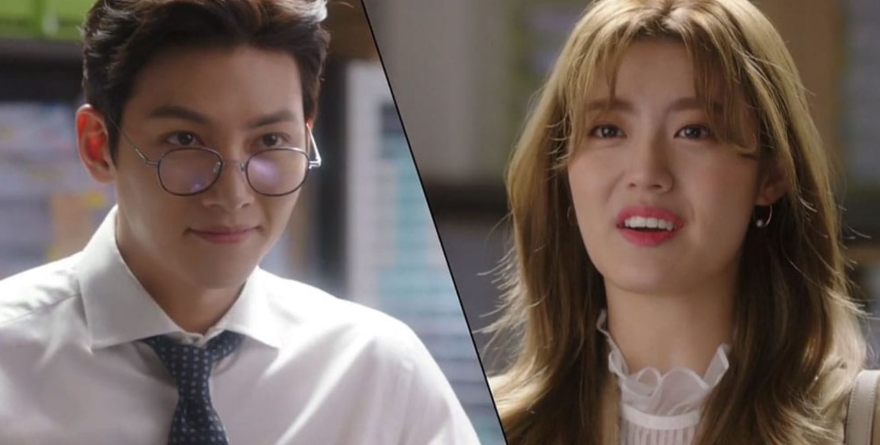 A close-up scene from Suspicious Partner, featuring the male lead wearing glasses and giving a playful smile, while the female lead looks at him with a surprised expression, set in a work environment. 
