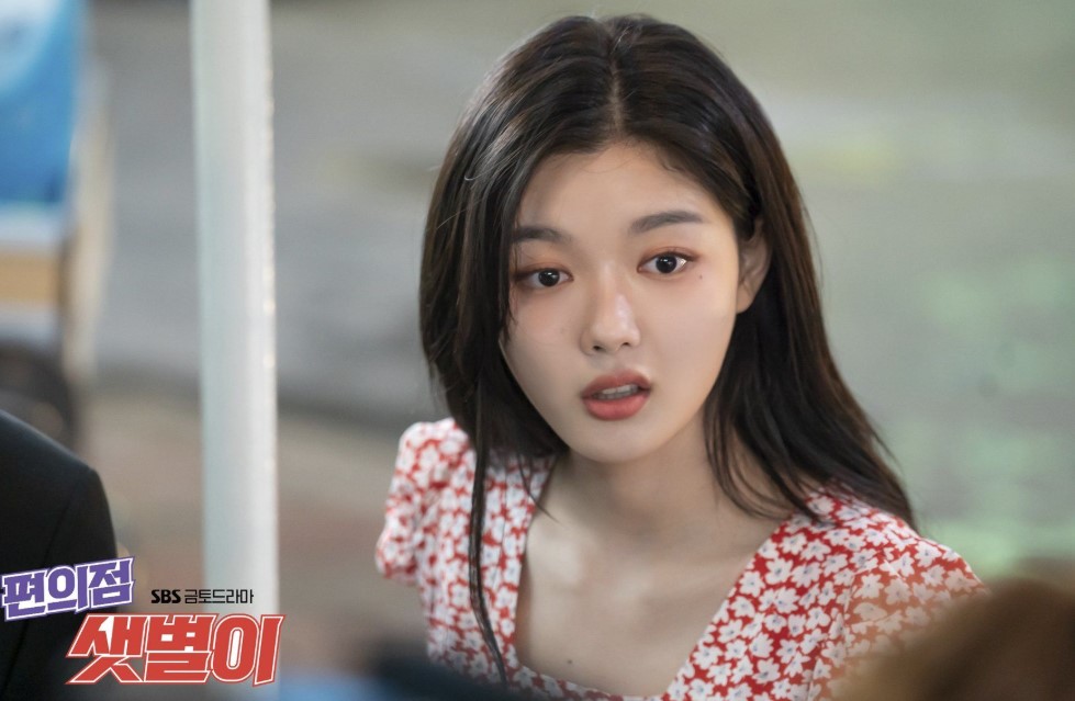 Kim You-Jung in a pivotal scene from 'Backstreet Rookie,' wearing a red floral dress and displaying a surprised expression. Her character, Jung Saet-Byul, is captured in a moment of emotion, highlighting her charm and personality in the romantic K-drama series.