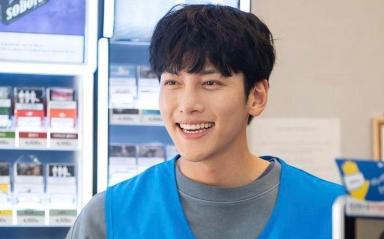 "Ji Chang-Wook smiling brightly while working at the convenience store in 'Backstreet Rookie,' wearing a blue vest. The cheerful moment highlights his character's friendly and approachable nature in the K-drama series.