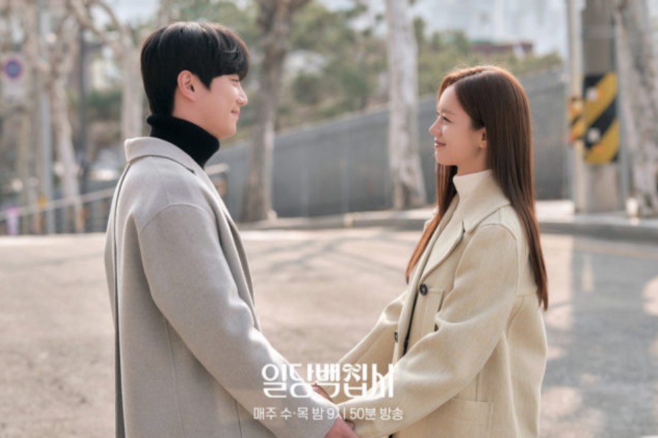 Couple holding hands and smiling at each other in a romantic outdoor scene from a Korean drama.