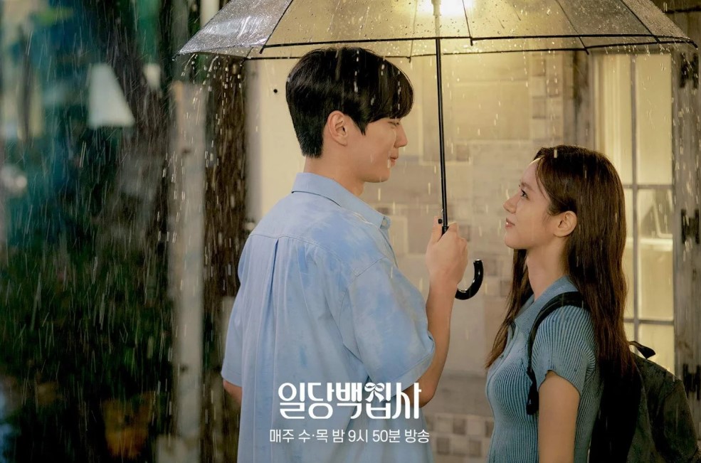 Couple standing under an umbrella in the rain, looking into each other's eyes in a romantic moment from a Korean drama.