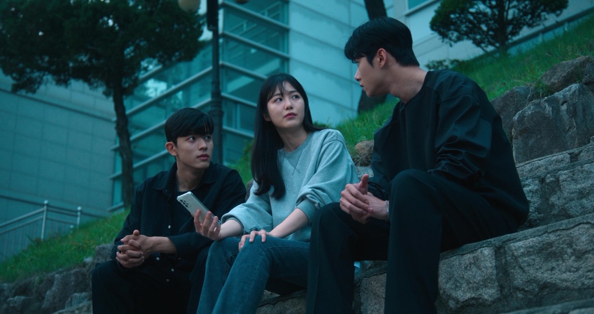 Three characters from 'Revenge of Others' sitting on a stone bench outdoors, with the woman in the middle holding a smartphone, while the two men on either side engage in a serious conversation.