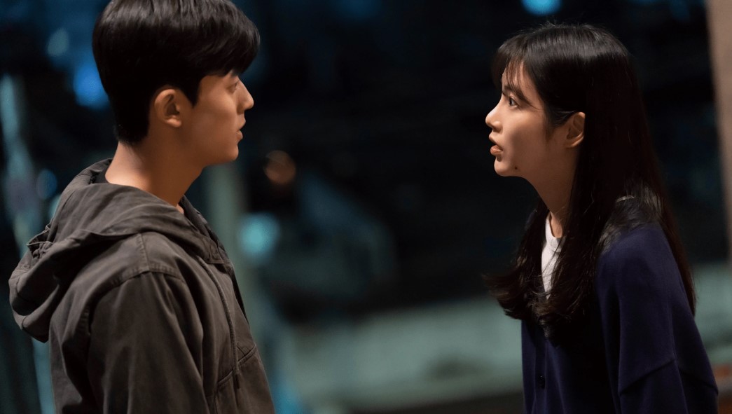 Intense confrontation between two characters from 'Revenge of Others,' with the male character in a hoodie facing the female character, who appears to be engaged in a serious conversation, set against a blurred nighttime background.