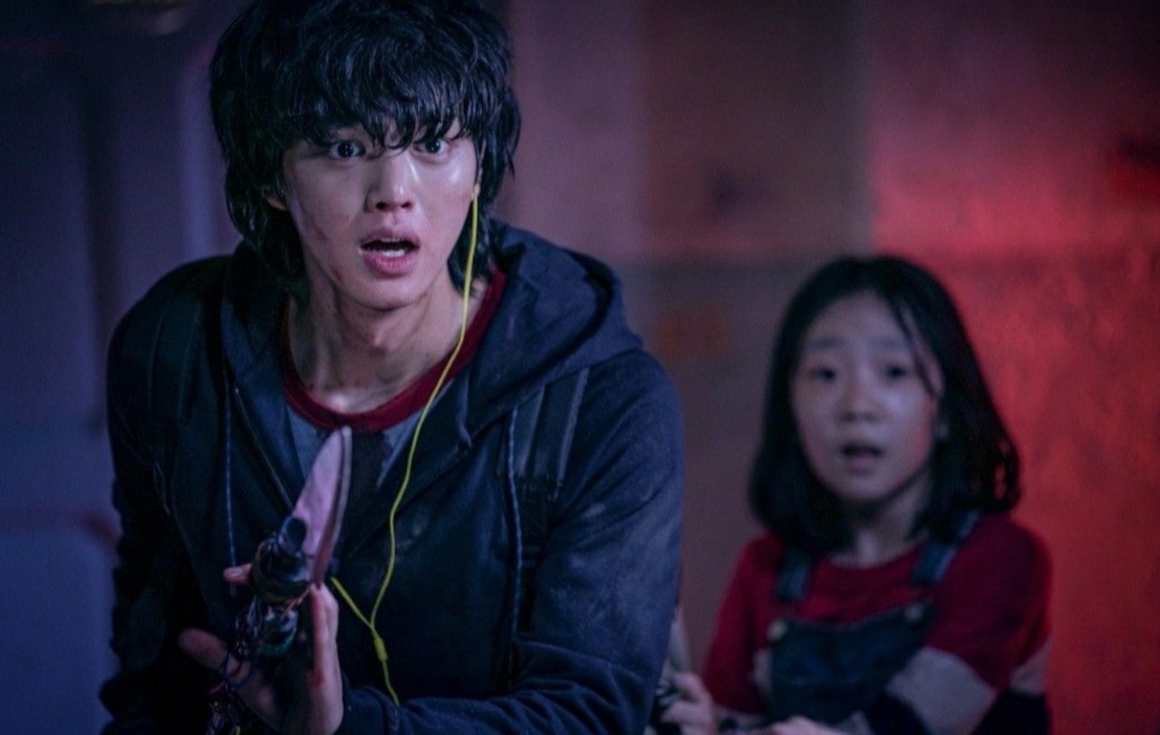 Scene from Sweet Home with a young man holding a weapon and looking terrified, while a young girl behind him is also frightened, both trapped in a dangerous situation.