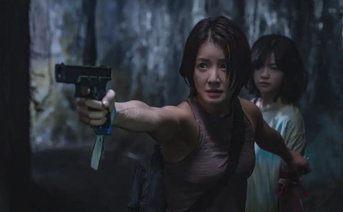 Character from Sweet Home Season 2 aiming a gun while protecting another character, set in a dark, eerie environment with intense focus.