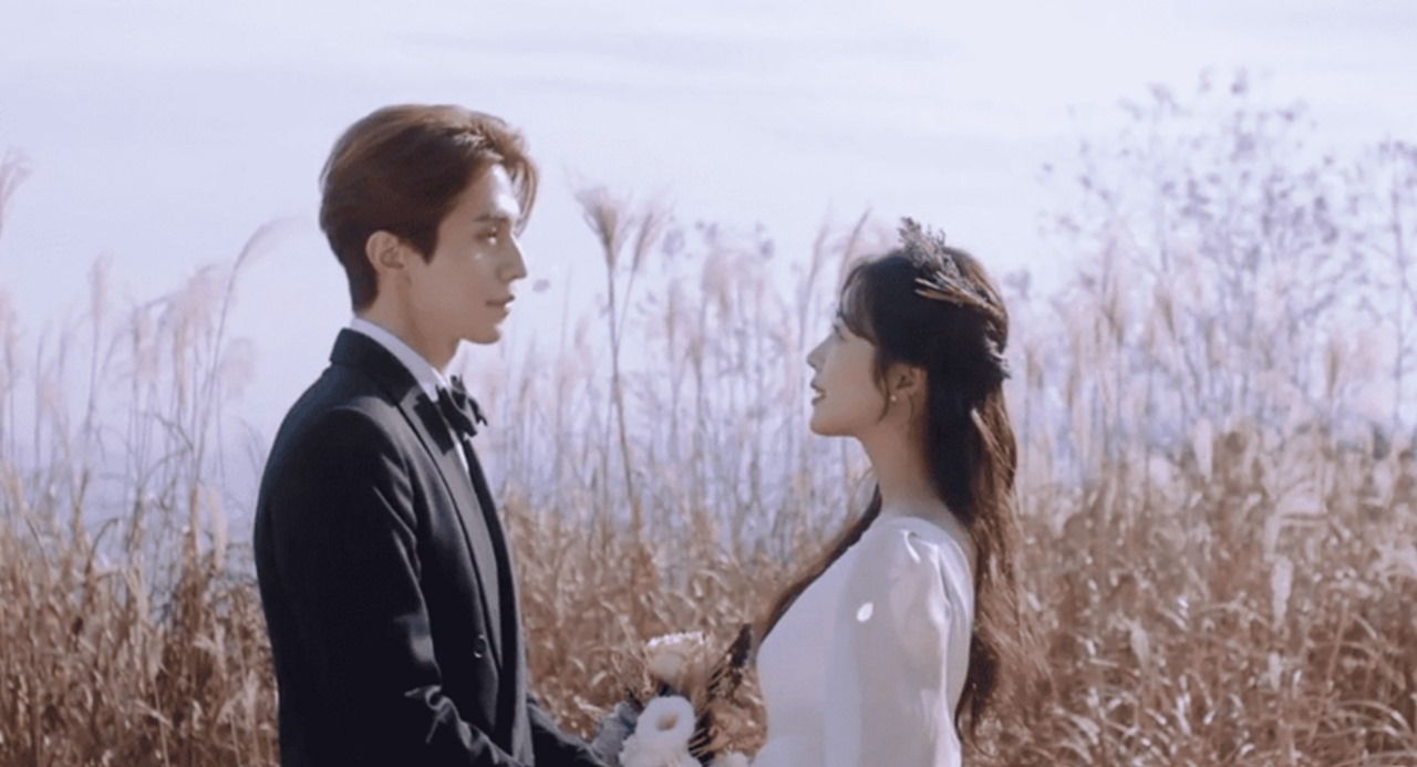 Romantic scene from 'Tale of the Nine-Tailed,' featuring Lee Dong-wook in a tuxedo and Jo Bo-ah in a white gown, sharing a tender moment in a scenic field.