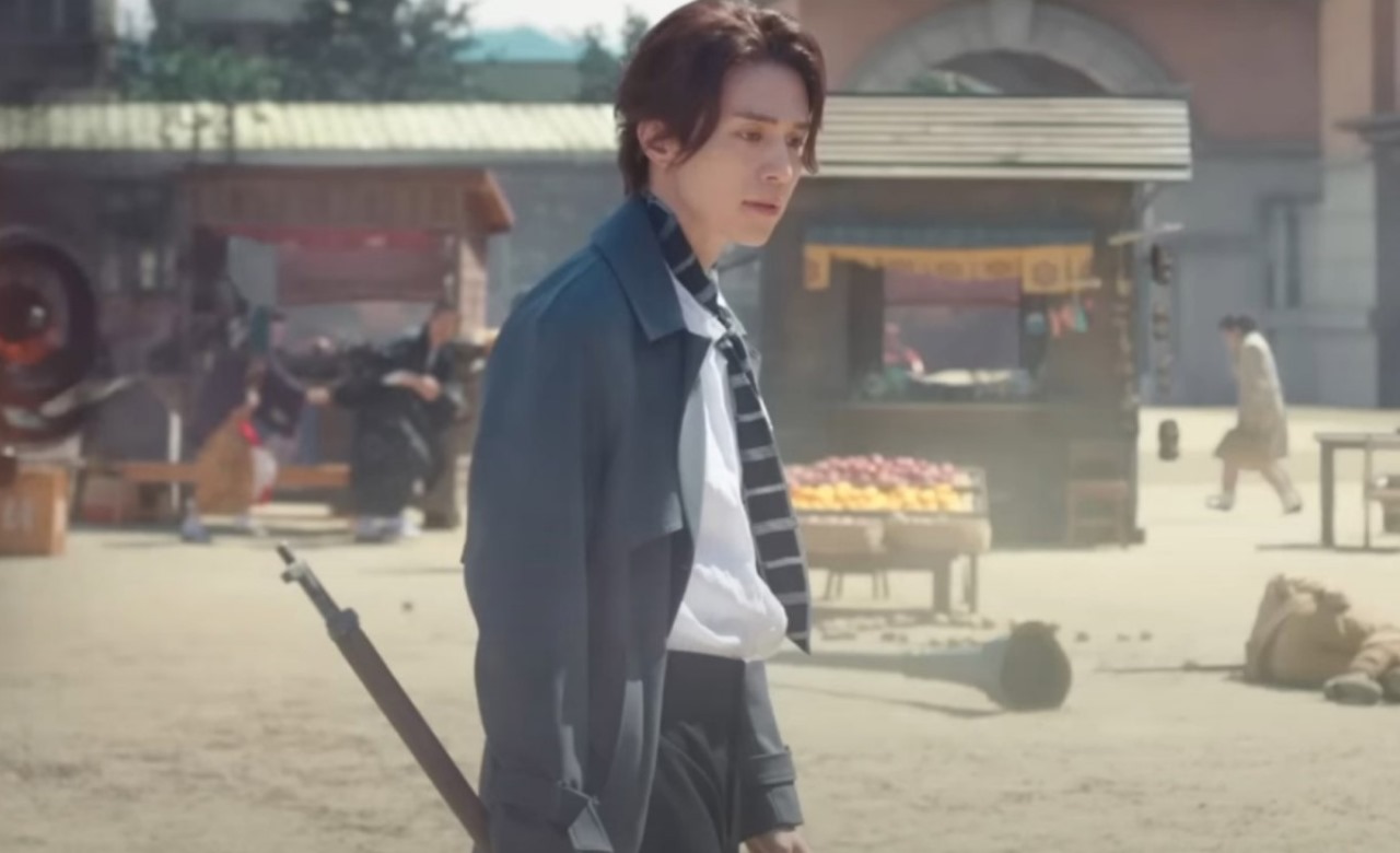 Scene from the South Korean drama 'Gumiho: 1985' featuring a male character walking through a vintage marketplace, holding a sword with a focused expression, set in an old-fashioned street environment.
