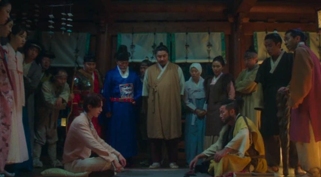 Scene from the South Korean drama 'Gumiho: 1985' featuring a group of characters dressed in traditional attire, gathered around a man sitting on the floor in a tense moment, set in an ancient Korean-style interior.