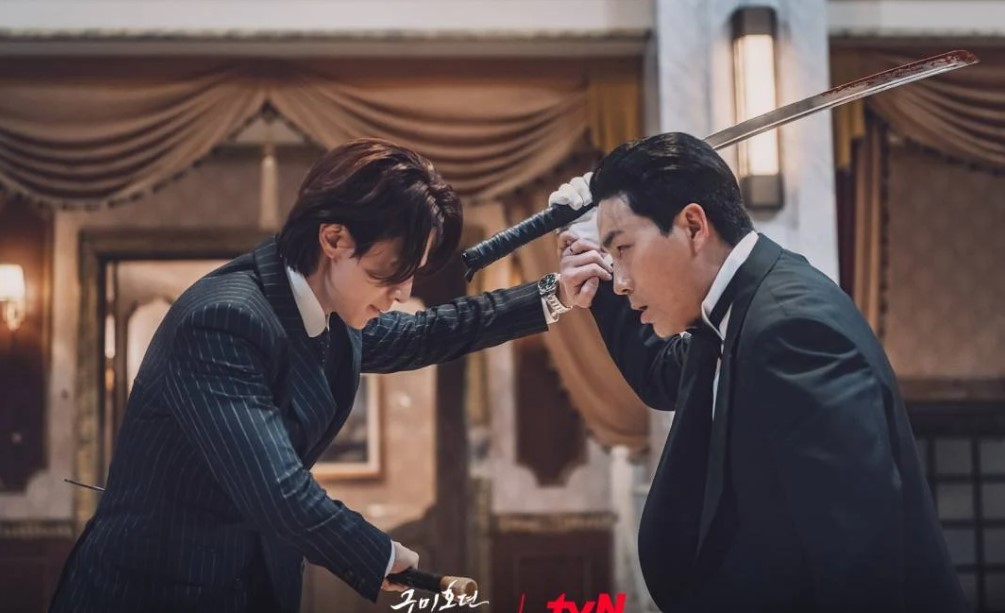 Intense fight scene from the South Korean drama 'Gumiho: 1985' showing two male characters in formal attire, one holding a sword and the other blocking it, set in an opulent interior.