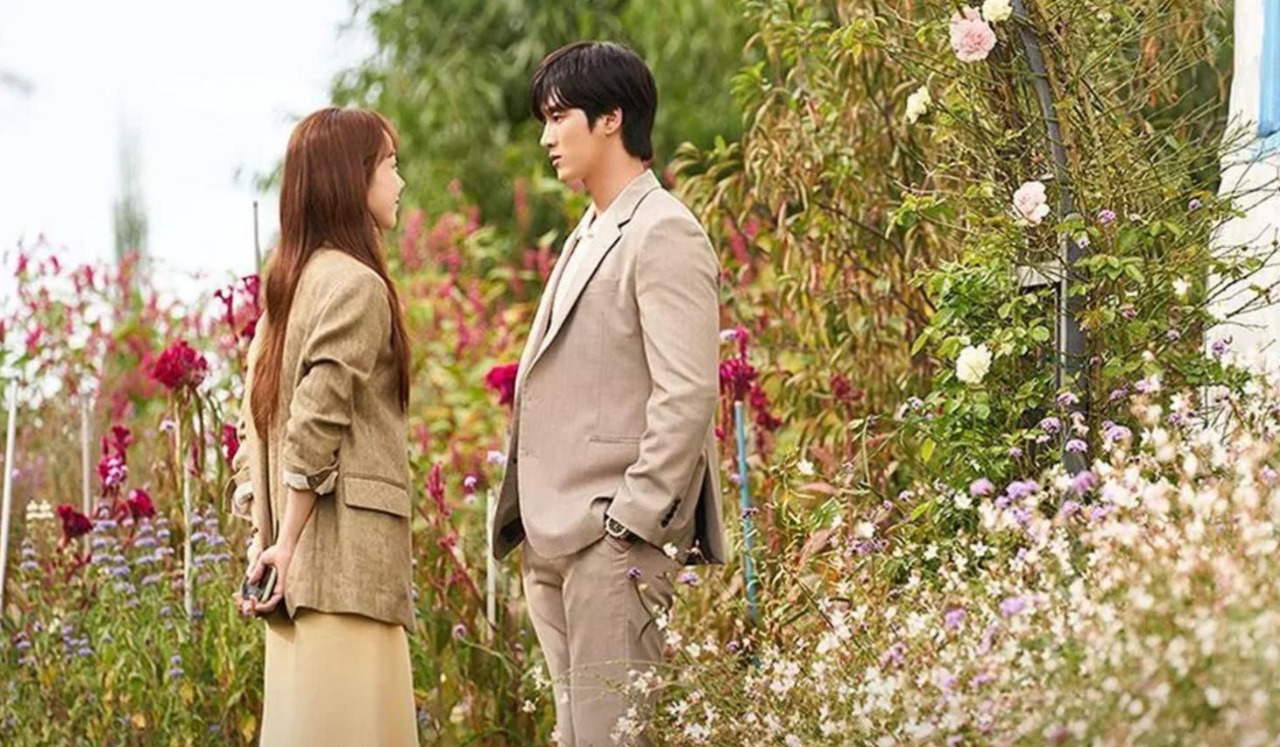 Romantic scene from 'This Life, Too, is Good,' showing the lead characters standing amidst a beautiful garden of colorful flowers, capturing a tender moment of connection and contemplation.