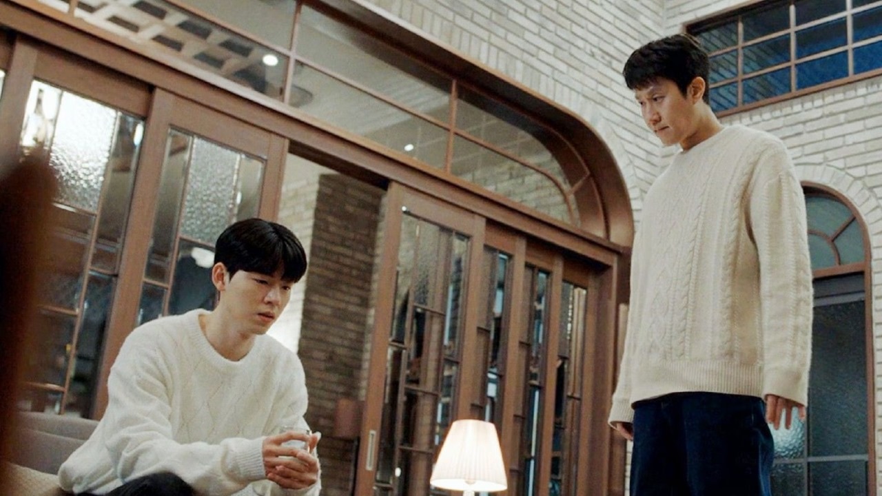 Emotional scene from 'Miraculous Brothers' with two characters in white sweaters, one seated and the other standing, creating a tense moment.
