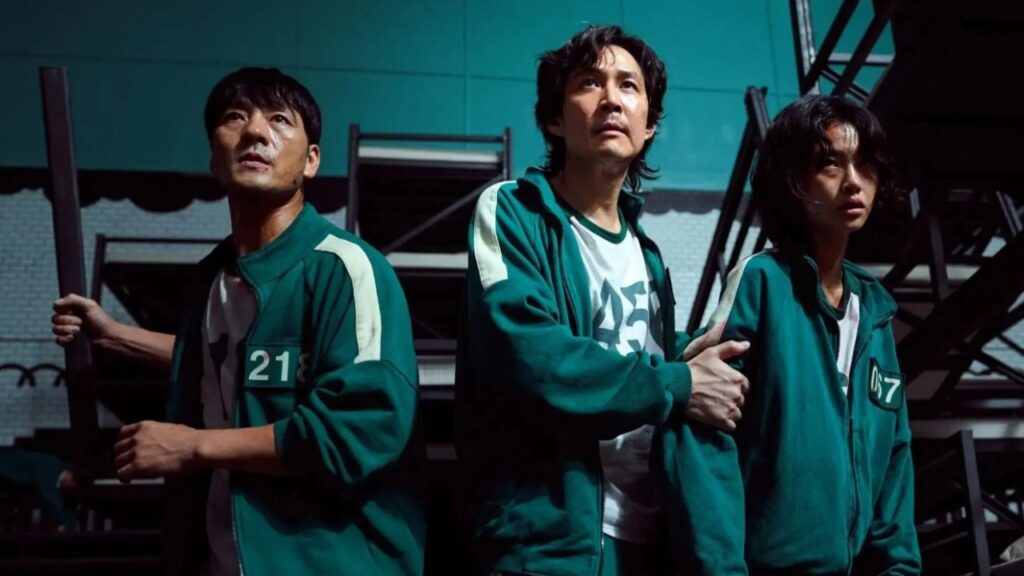 Characters from Squid Game Season 1, including players wearing green tracksuits with numbers 21, 218, and 07, show intense expressions as they navigate a tense moment. The image highlights their vulnerability and suspense in the high-stakes game, making it perfect for a Squid Game season 1 full review.