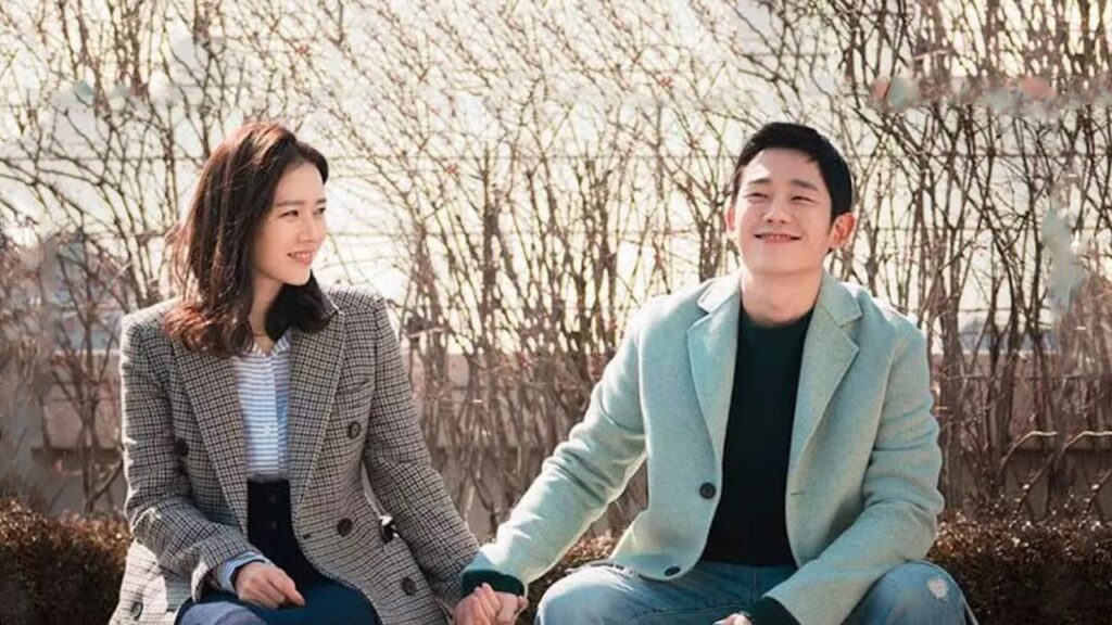 Scene from the K-drama "One Spring Night" showing a smiling couple sitting on a bench holding hands, with bare trees in the background. Discover more about this series on Top Honest KDrama Review Sites.