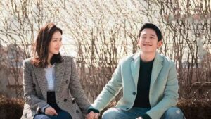 Scene from the K-drama "One Spring Night" showing a smiling couple sitting on a bench holding hands, with bare trees in the background. Discover more about this series on Top Honest KDrama Review Sites.