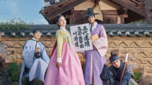 The cast of "My Secret Romantic Guesthouse" dressed in traditional Korean hanbok poses in front of a historic Korean house. The image beautifully captures the period setting and character dynamics of the drama. Ideal for use in My Secret Romantic Guesthouse full review.
