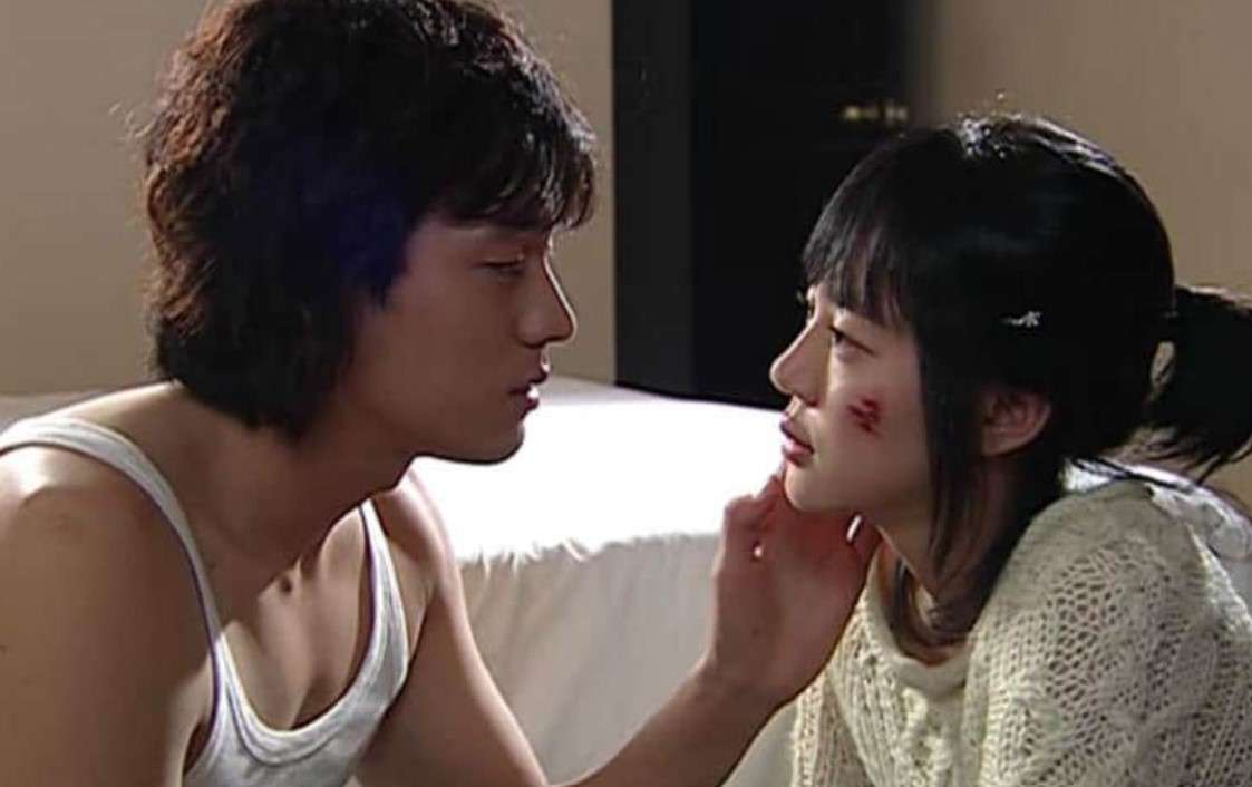 A young man and woman who is hurt are seated beside a bed, smiling and enjoying each other's company in a cozy setting.