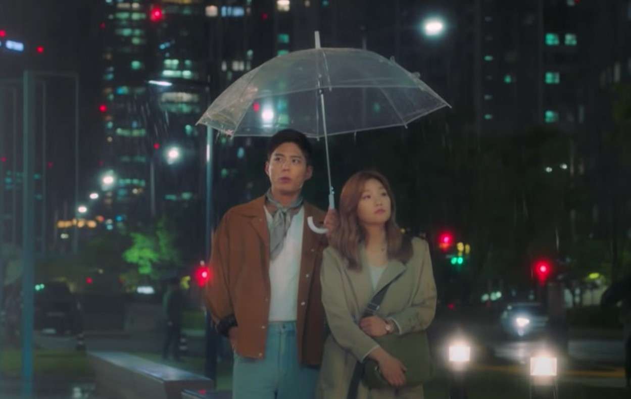 Sa Hye-jun (Park Bo-gum) and Ahn Jeong-ha (Park So-dam) walking together under an umbrella on a rainy night in a romantic scene from 'Record of Youth.