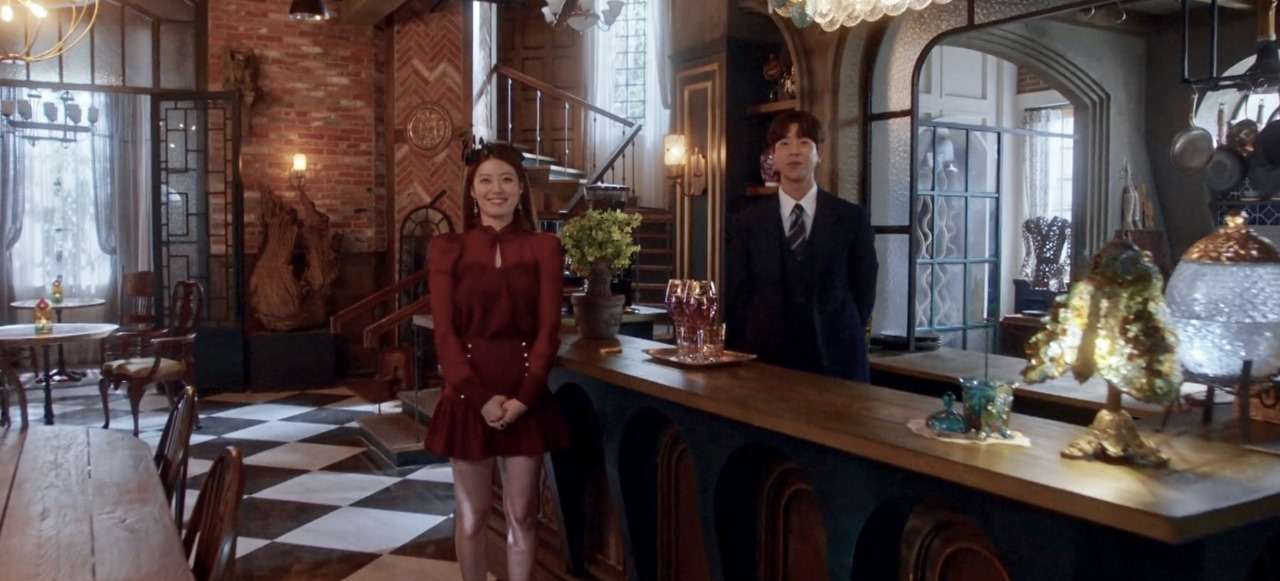 Scene from 'The Witch’s Diner' featuring two main characters standing in the cozy, mystical restaurant interior, with elegant decor and a vintage-style bar, creating an enchanting atmosphere.