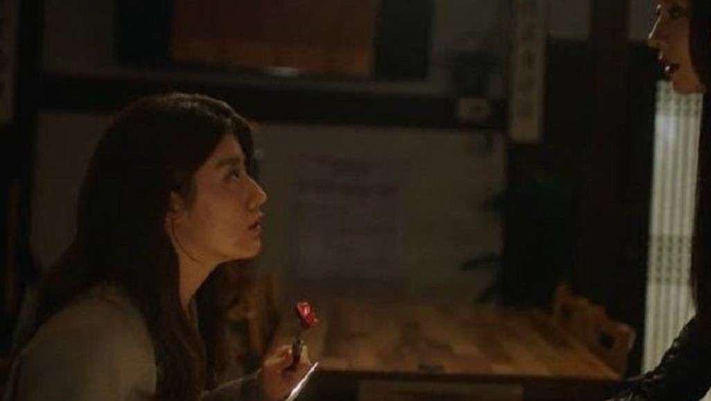 Scene from 'The Witch’s Diner' showing a tense moment between two characters, with one holding a rose lollipop and looking up in anticipation, set in a dimly lit, mysterious environment.