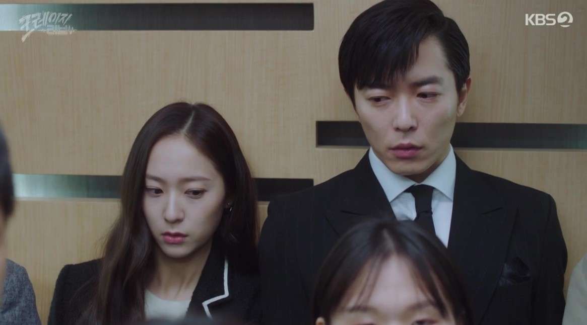 Scene from 'Crazy Love' showing the lead characters standing side by side in an elevator, both with serious expressions, capturing a tense and intimate moment.