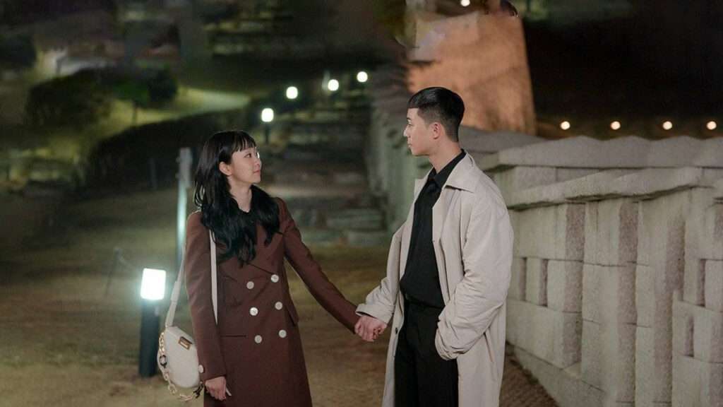 A man and woman clasp hands in front of a wall, highlighting their connection in "Itaewon Class," included in Most-Streamed KDrama Soundtracks.